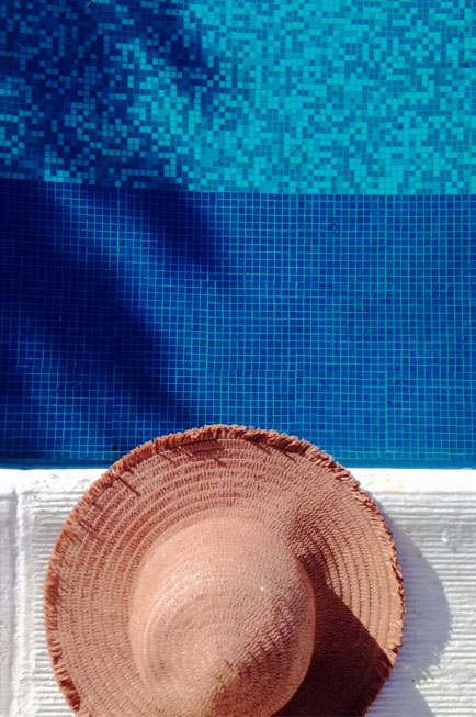 Chapeau en paille sur le bord de la piscine et mosaïque bleue foncée et claire avec reflet d'un palmier dans l'eau pour illustrer que Destination Piscine Horizon ce sont des créateurs de moments