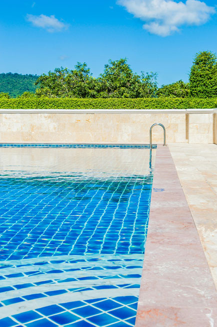 Piscine avec revêtement bleu réfléchissant la lumière, escalier intégré et beau jardin vert avec des arbres en arrière-plan